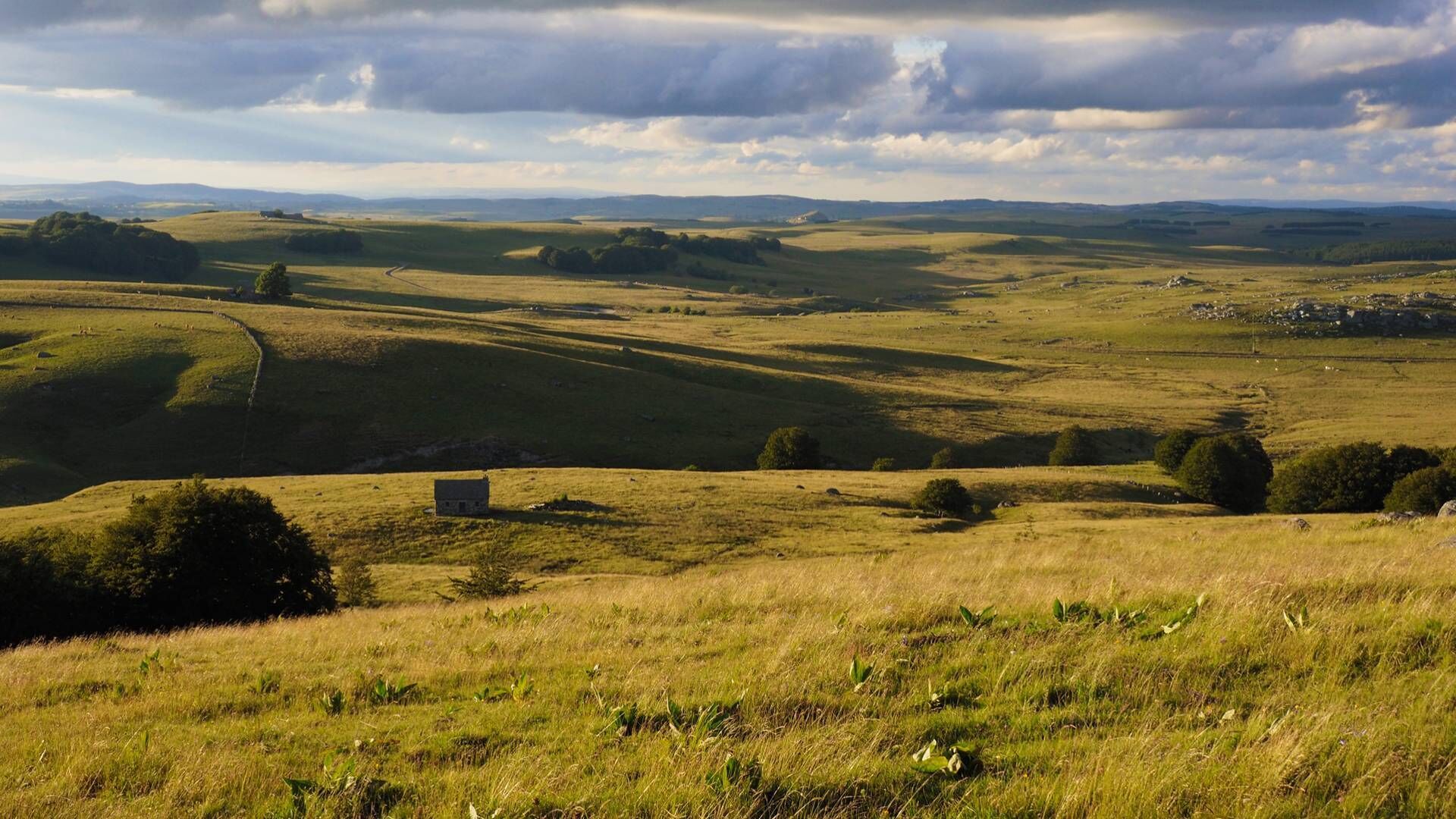 A panoramic view of rolling hills with a small building in the foreground.