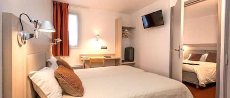 A hotel room with a large bed, a desk, a TV, and a wardrobe.