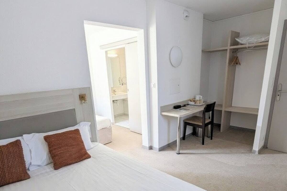 Ein Hotelzimmer mit einem großen Bett, einem Schreibtisch und einem Stuhl. Eine Tür führt zu einem Badezimmer und es gibt einen Schrank.
