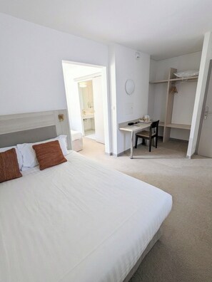 Ein Hotelzimmer mit einem großen Bett, einem Schreibtisch und einem Stuhl. Eine Tür führt zu einem Badezimmer und es gibt einen Schrank.