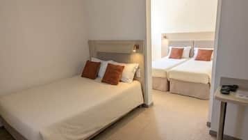 A hotel room with a single bed, a second bed, a small table, and a window.