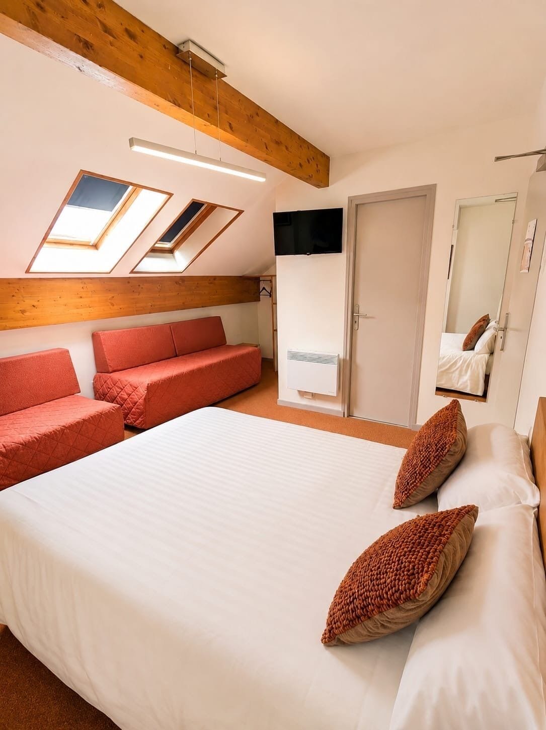 A bedroom with a large bed, a red sofa, a TV, and skylights.