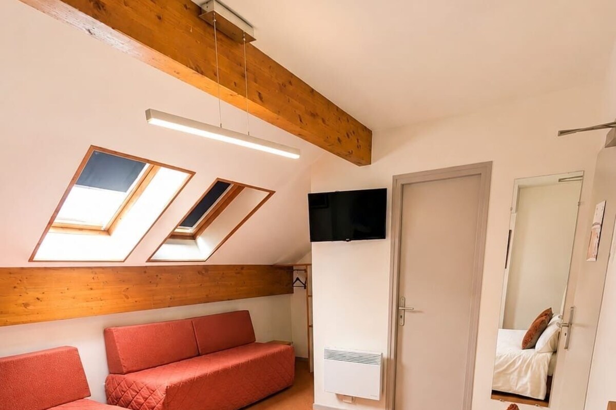 Quarto com uma cama grande, um sofá vermelho, uma televisão e claraboias.