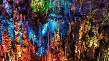 Gedetailleerd uitzicht op een grot met kleurrijke stalactieten en -stalagmieten, verlicht door kunstmatige verlichting.