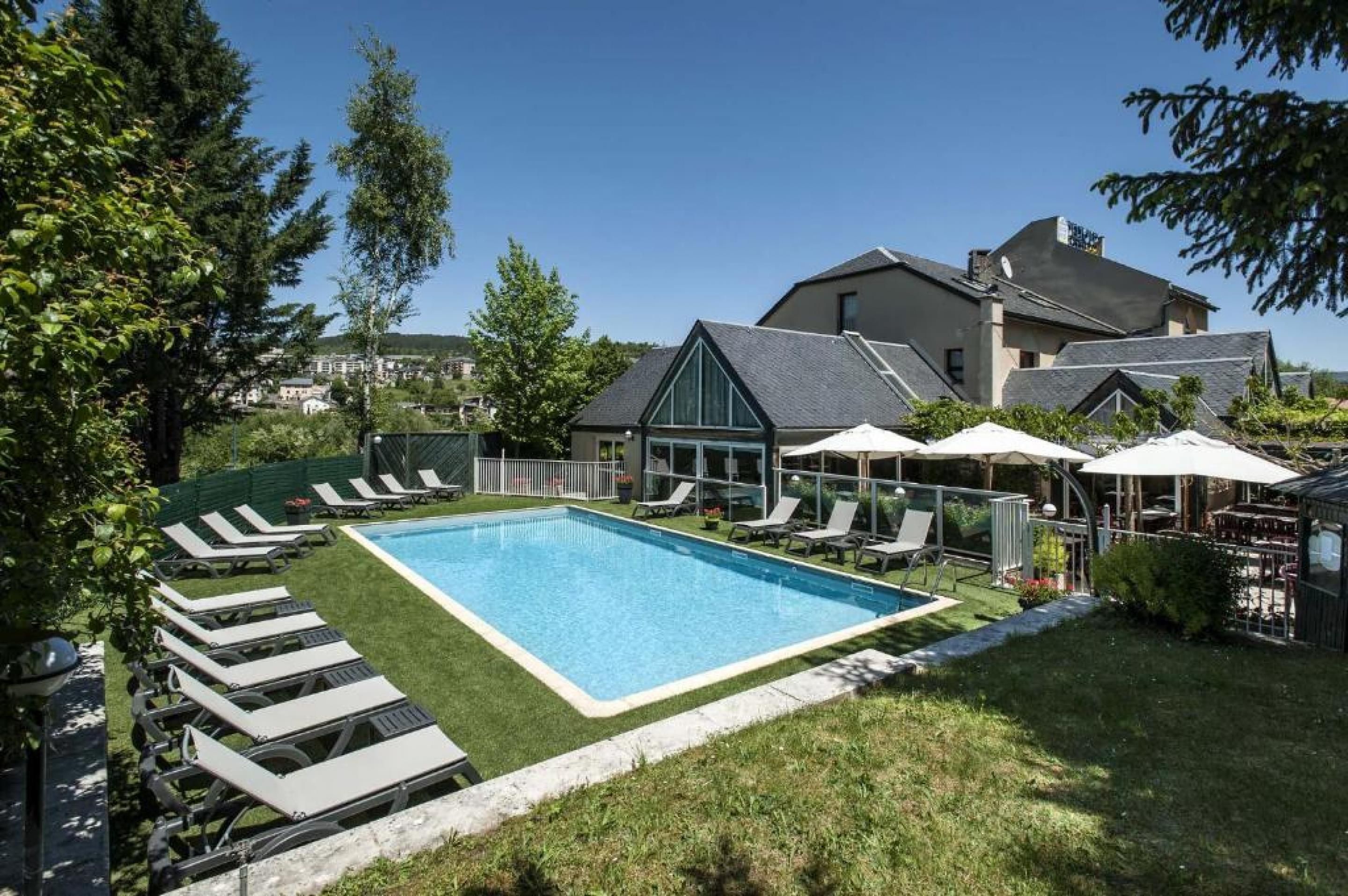 A swimming pool with lounge chairs and umbrellas, surrounded by a grassy area and trees.