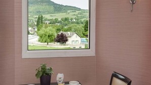 Een eetgedeelte met een tafel voor twee personen, een raam met uitzicht op een groen landschap en een wandlamp.