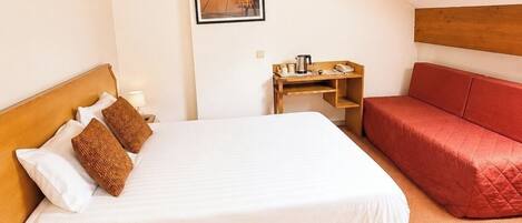 Un dormitorio con cama, un sofá rojo, una mesita de noche de madera, un cuadro en la pared y un techo inclinado.