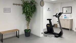 Een kamer met een loopband, een potplant, een bankje, een klok, een klein plankje met een plant, en een spiegel aan de muur.
