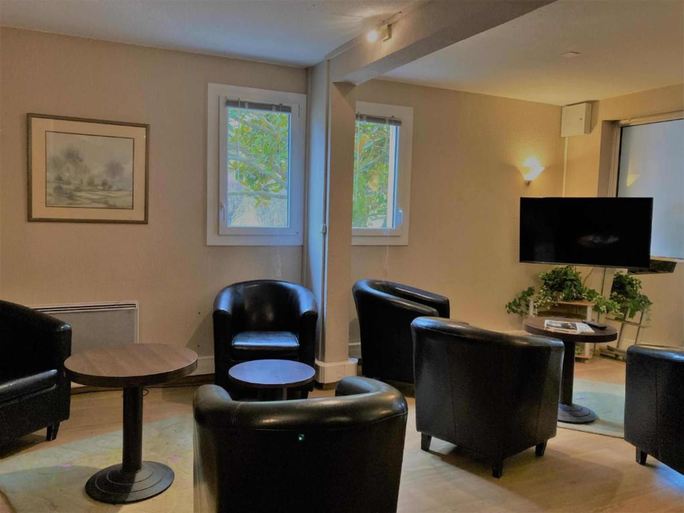 Une pièce comprenant un canapé en cuir noir, une petite table ronde et un téléviseur fixé au mur.