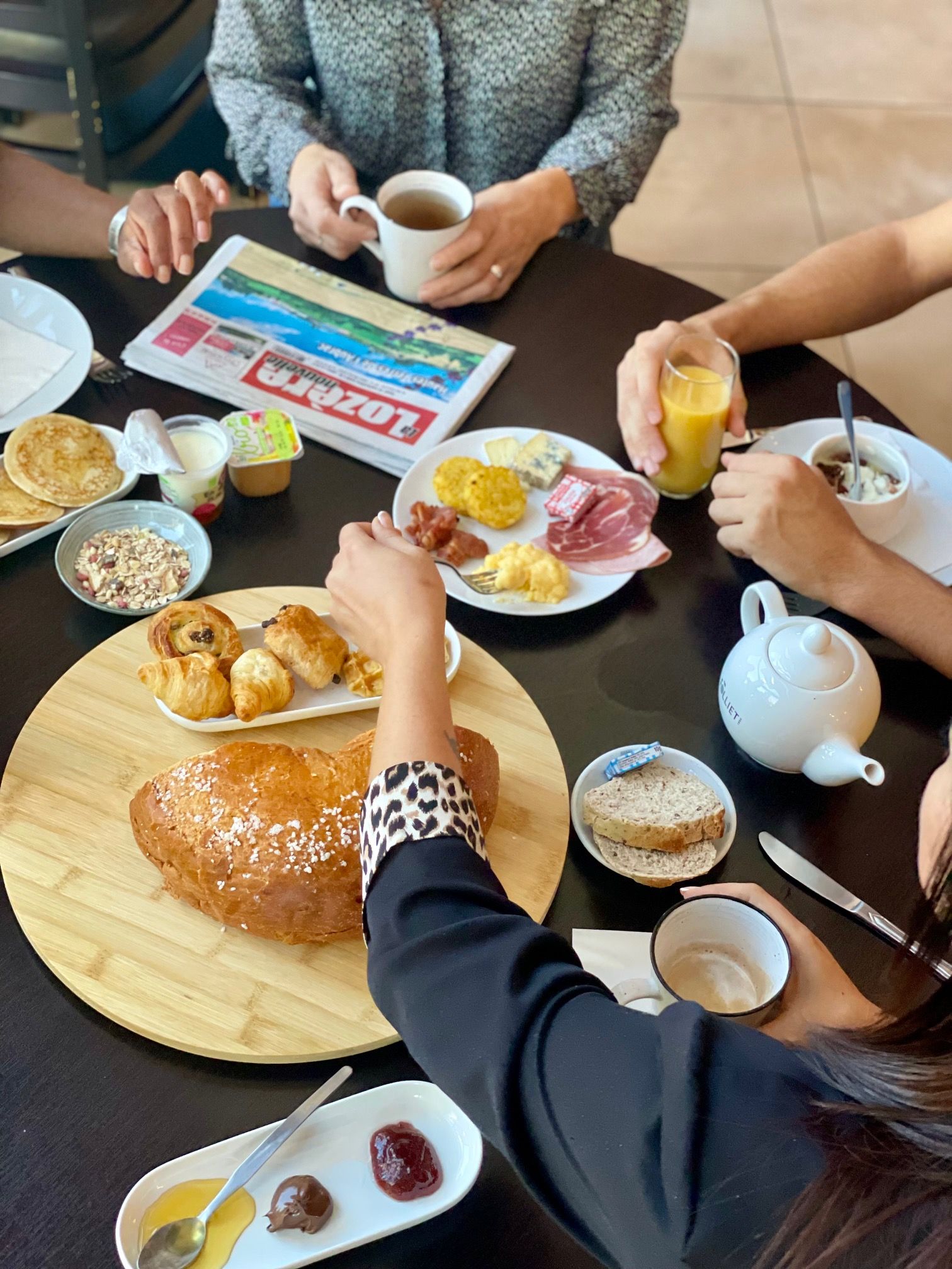 Un desayuno con diversas opciones de comida sobre una mesa, incluyendo bollería, huevos y una tetera.