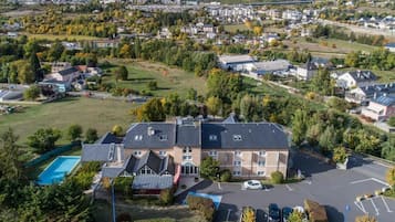 A hotel with a swimming pool, parking lot, and a view of the surrounding town.