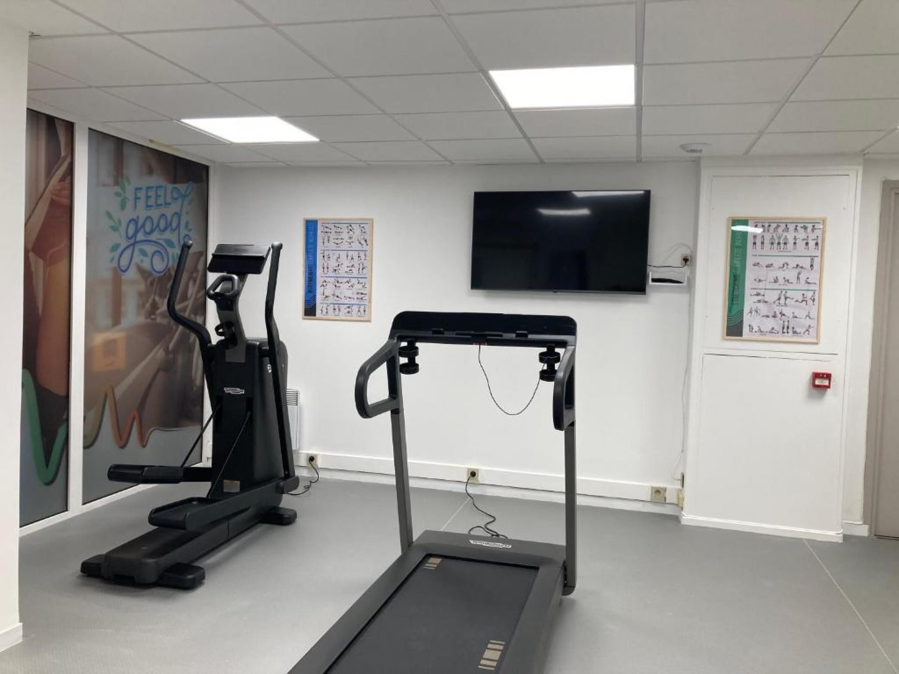 A fitness room with exercise equipment, a television, and motivational posters on the walls.