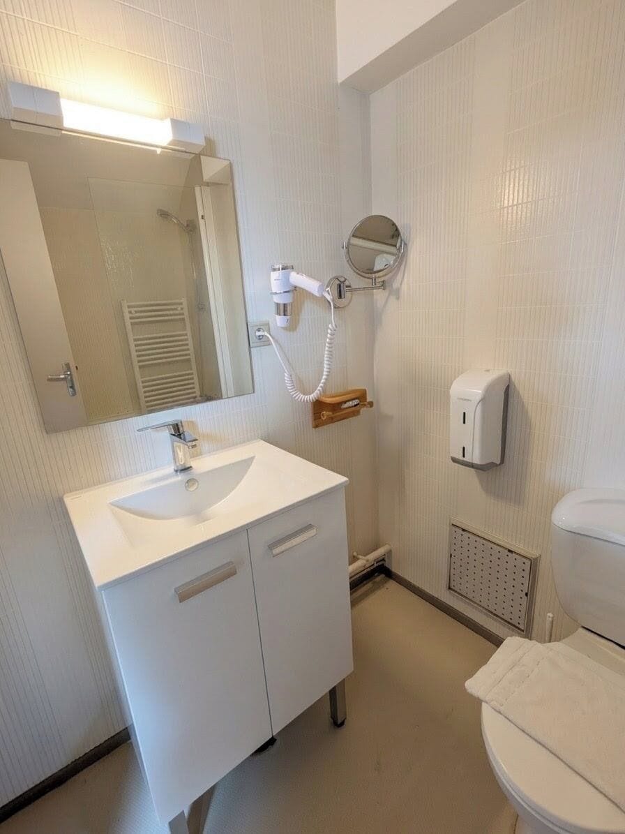 Ett badrum med ett vitt handfat, en spegel, en toalett och en handduksdispenser.