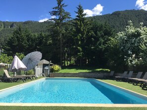 Een rechthoekig zwembad met helderblauw water, omringd door een gazon met ligbedden en parasols.