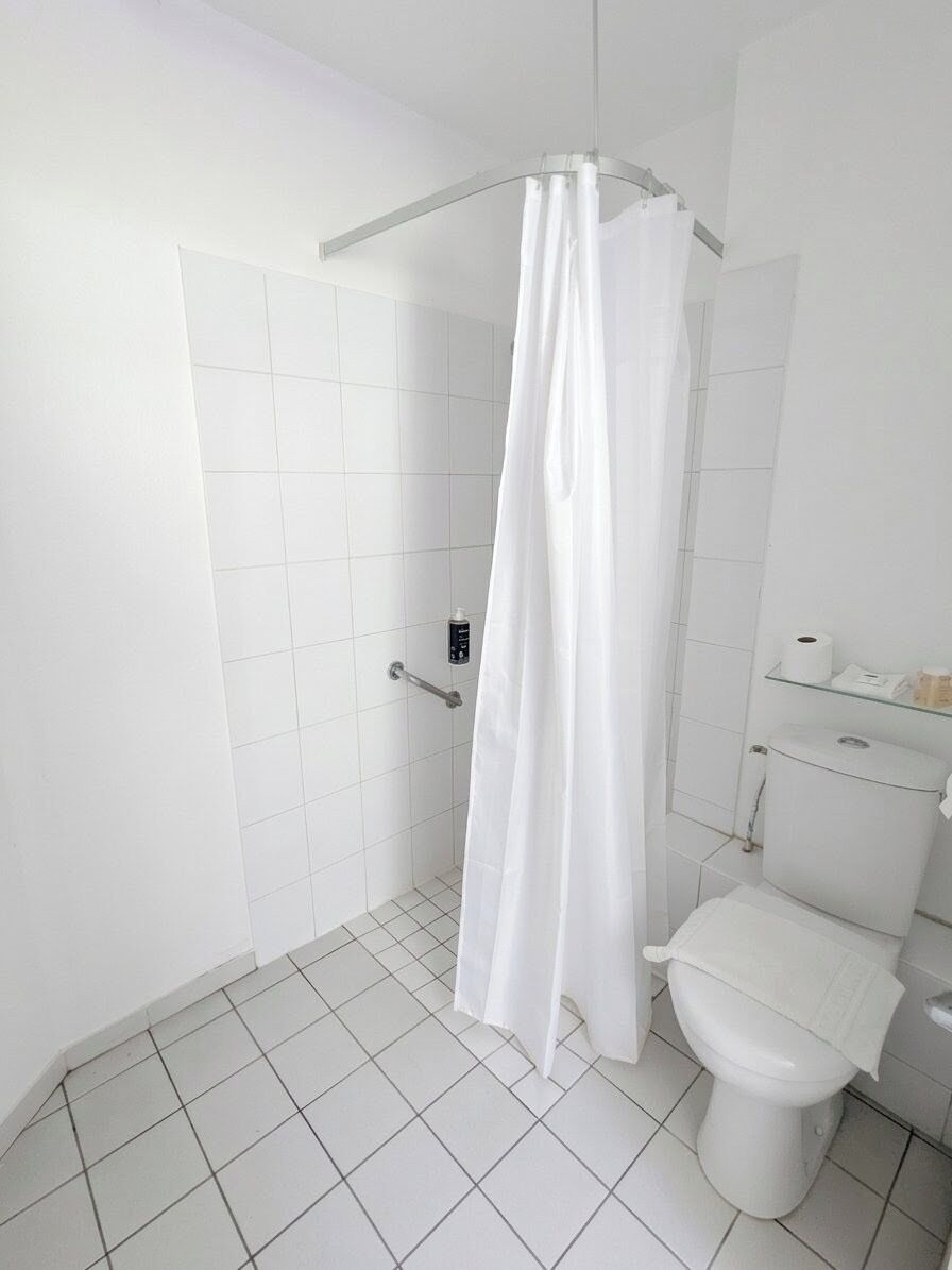 Un baño con ducha, inodoro y un estante con artículos de aseo.