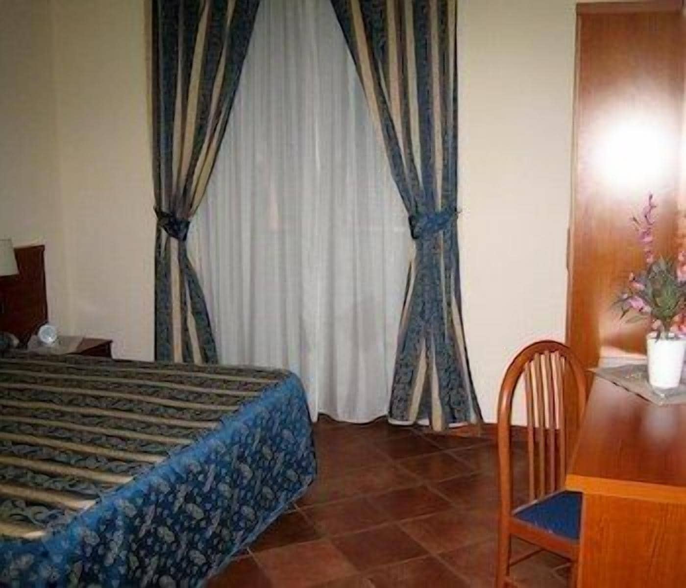 A hotel room with a bed, a wooden desk, a chair, and a potted plant.