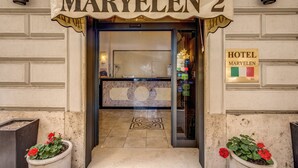 La entrada del Hotel Maryelen 2, con mostrador de recepción, un diseño decorativo en el suelo y plantas en macetas.