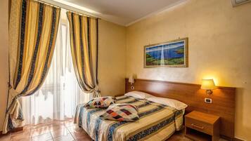 Una camera da letto con un letto, tende, un comodino, una lampada a parete e un quadro.