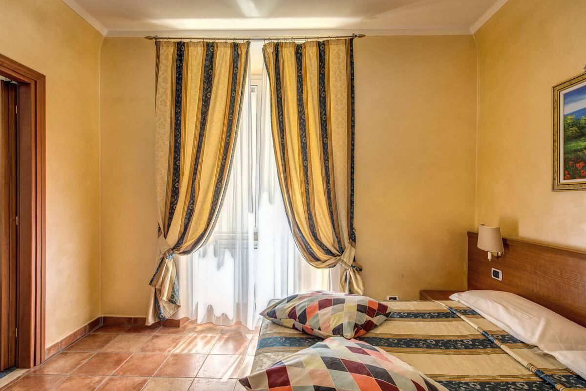 A hotel room with a bed, curtains, a painting, and a nightstand.