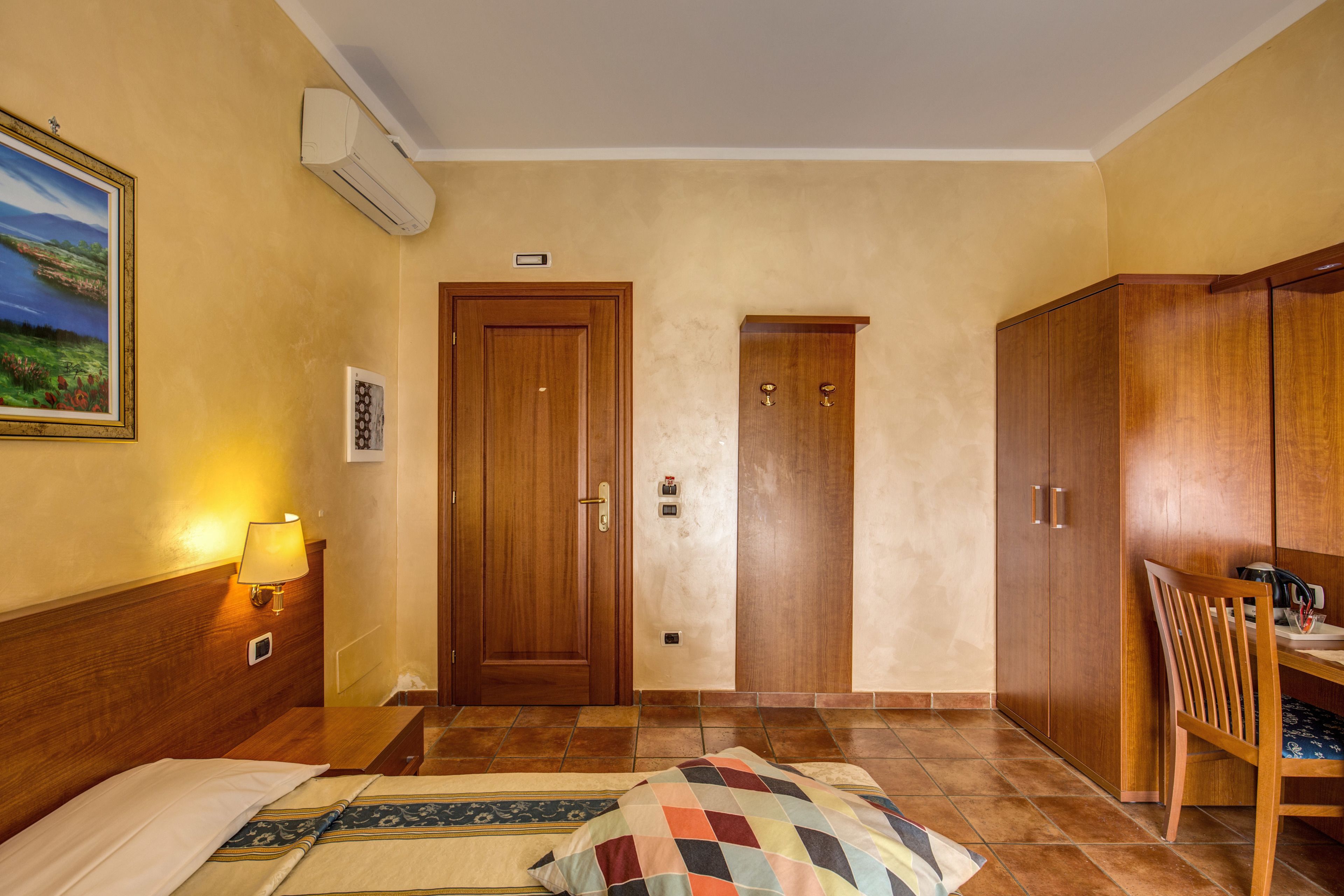A hotel room with a bed, a desk, a chair, a lamp, and a wardrobe.