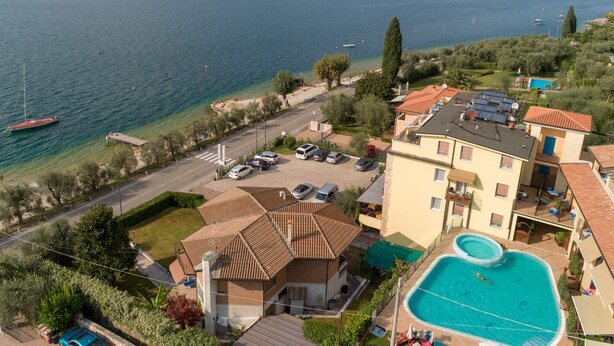 A residential area with a swimming pool, a road, and a view of the sea. - Hotel Rosmari (Brenzone sul Garda)