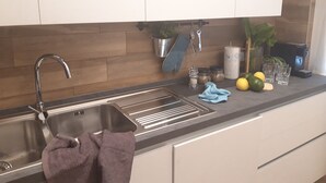 A modern kitchen with a stainless steel sink, wooden backsplash, and white cabinets. - Hotel Rosmari (Brenzone sul Garda)