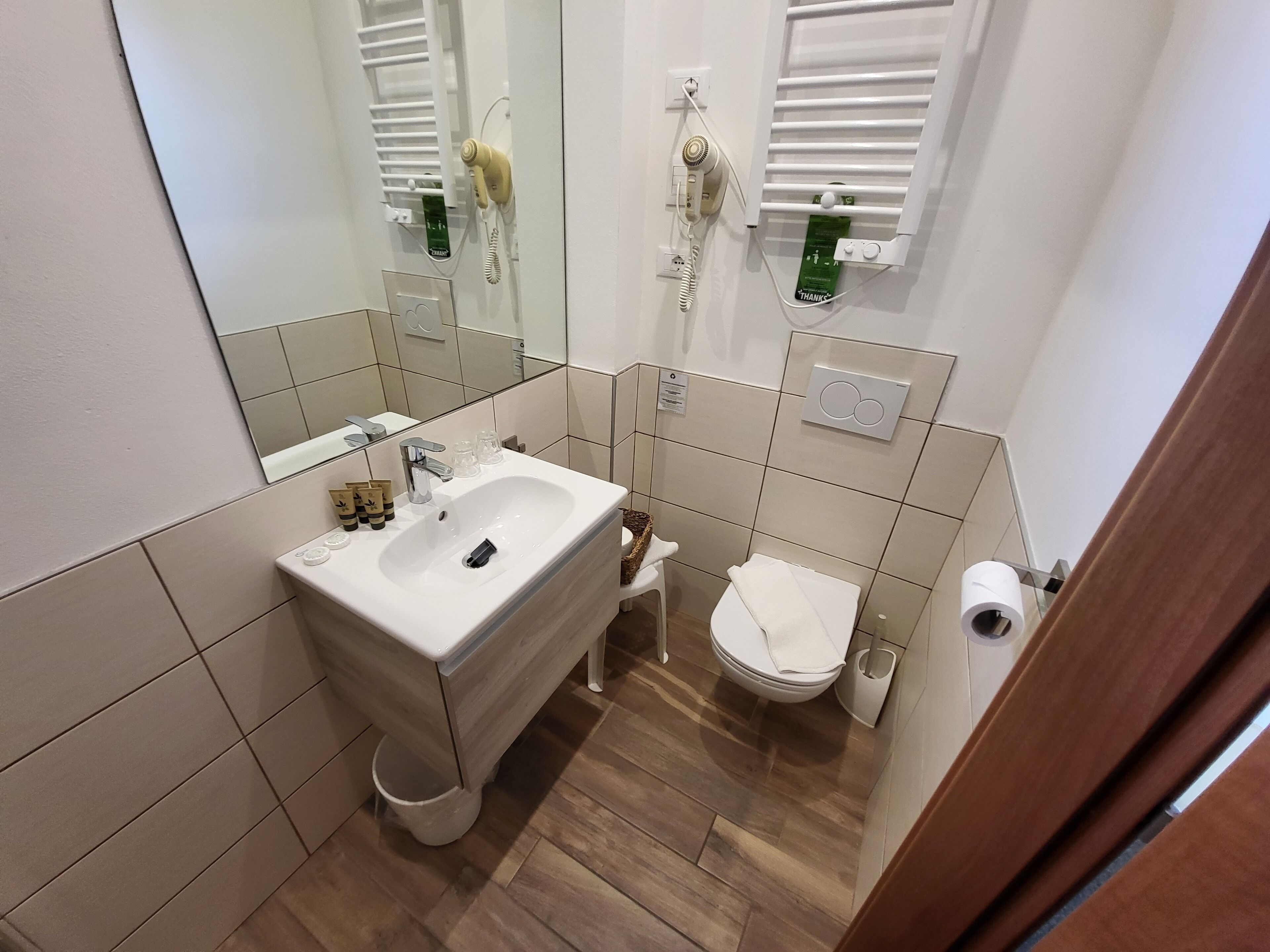 Ein Badezimmer mit Waschbecken, Toilette und Spiegel. Über der Toilette befindet sich ein Handtuchhalter und an der Wand ein Fön.