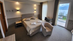 A modern hotel room with a large bed, a sitting area with a chair, a desk, and a balcony with a view of the water. - Hotel Rosmari (Brenzone sul Garda)