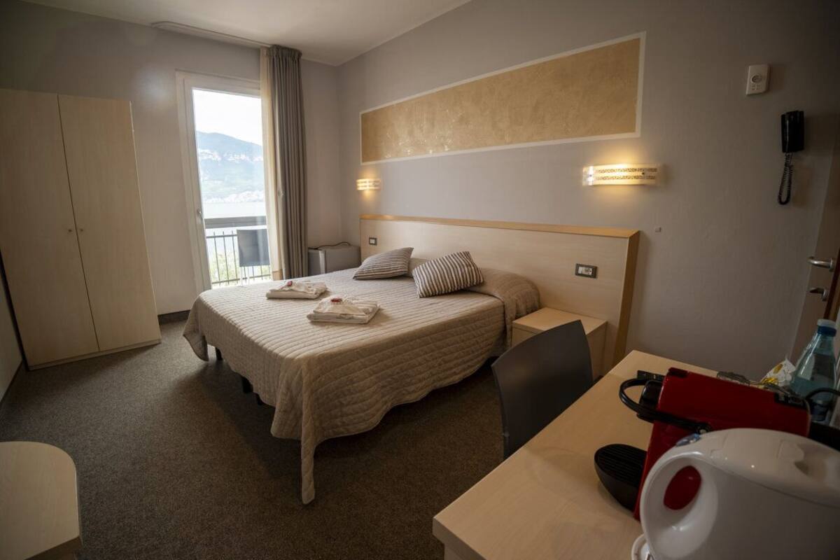 A hotel room with a bed, bedside tables, a desk, a chair, a telephone, and a window with a view of the outdoors.