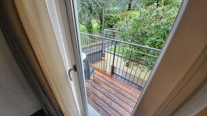 A view from a balcony with a wooden deck, metal railing, and greenery in the background. - Hotel Rosmari (Brenzone sul Garda)