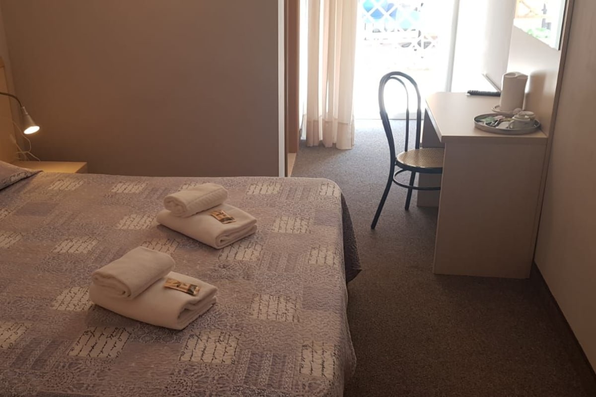 A hotel room with a bed, a desk, and a chair. There are towels on the bed.