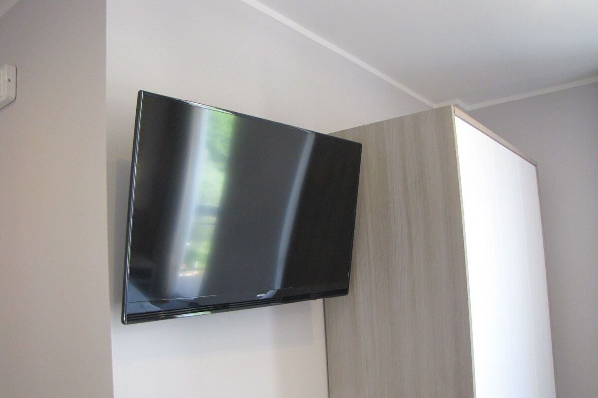 A flat-screen TV mounted on a wall in a room with light-colored walls and a wooden panel.