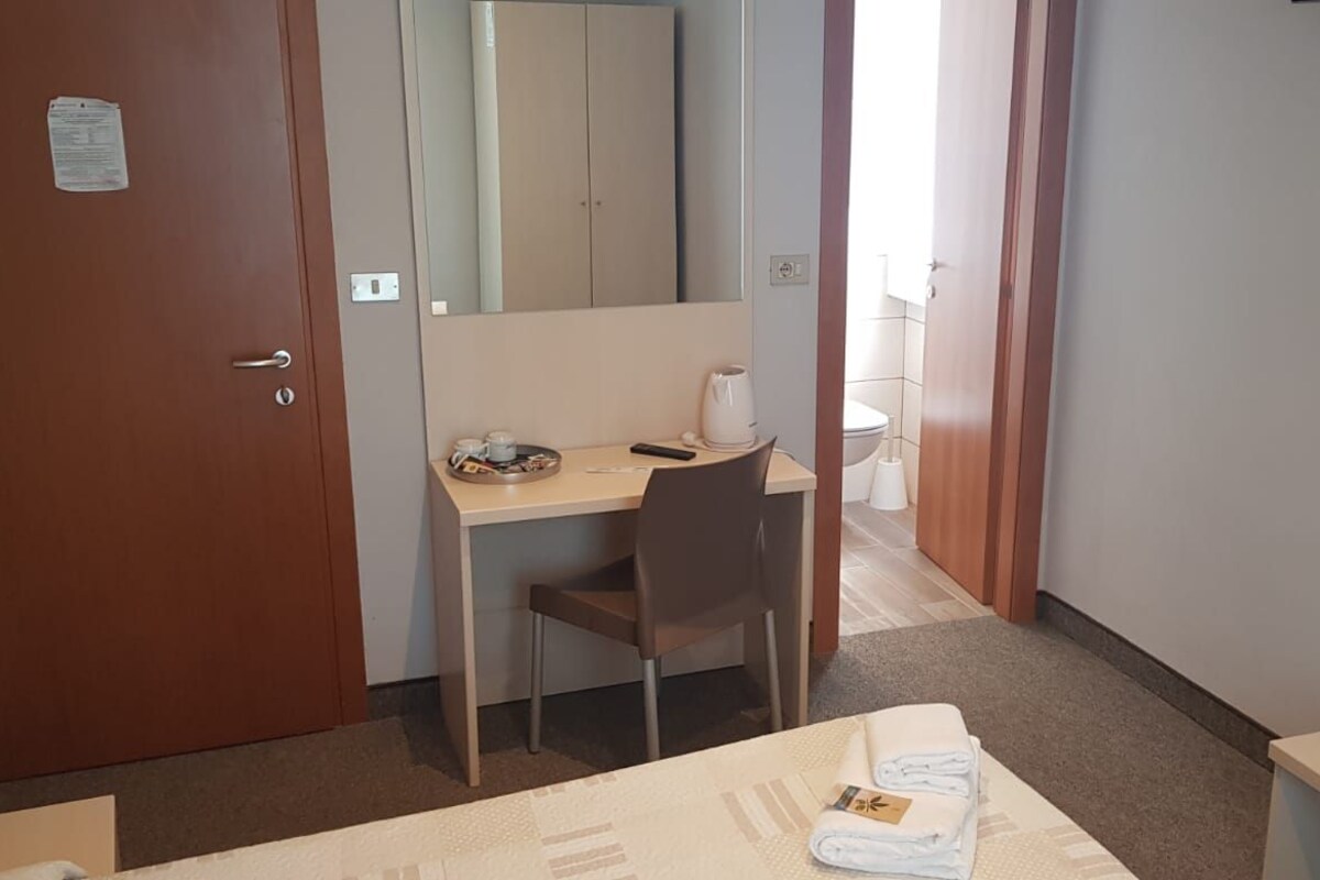 A hotel room with a desk, chair, and a bed with a neatly folded towel.