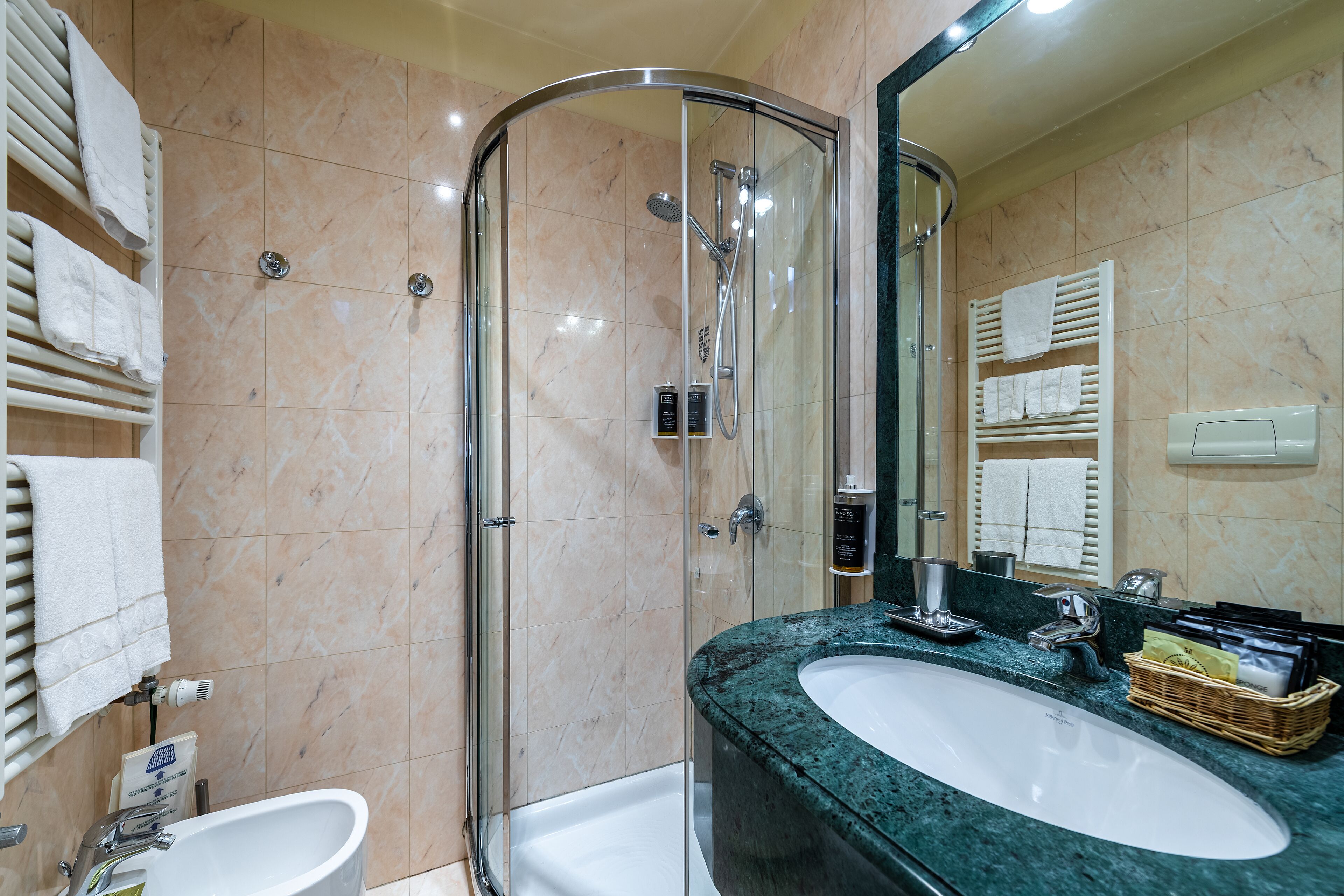 Un bagno moderno con cabina doccia in vetro, un lavandino bianco e una parete rivestita in marmo.