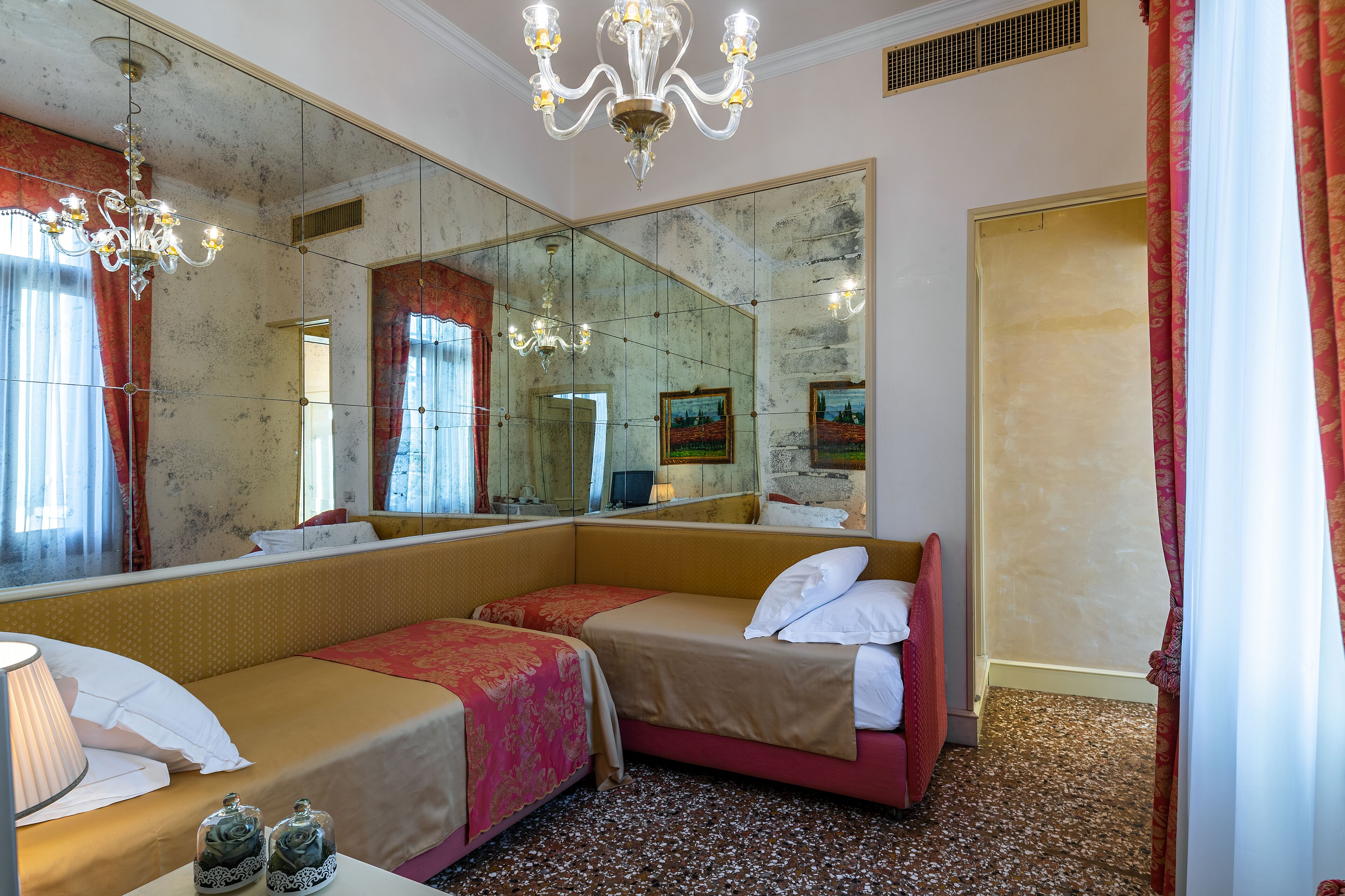 Camera d'albergo con due letti, un grande specchio, un lampadario e pavimento con moquette.