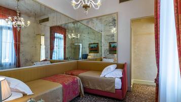 Camera d'albergo con due letti, un grande specchio, un lampadario e pavimento con moquette.