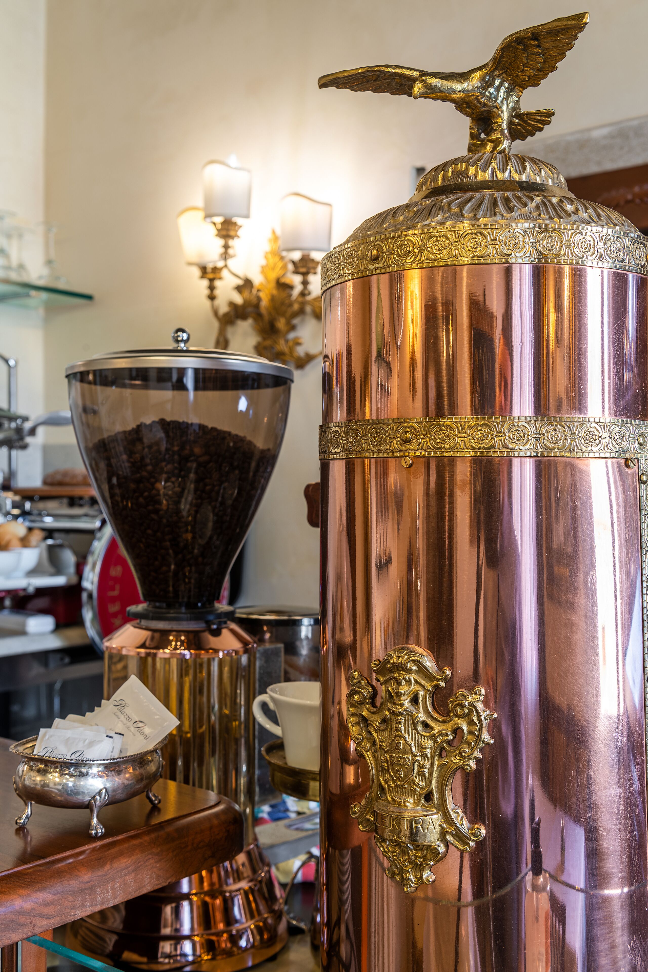 A metallic coffee grinder with a decorative eagle emblem and a coffee bean hopper.