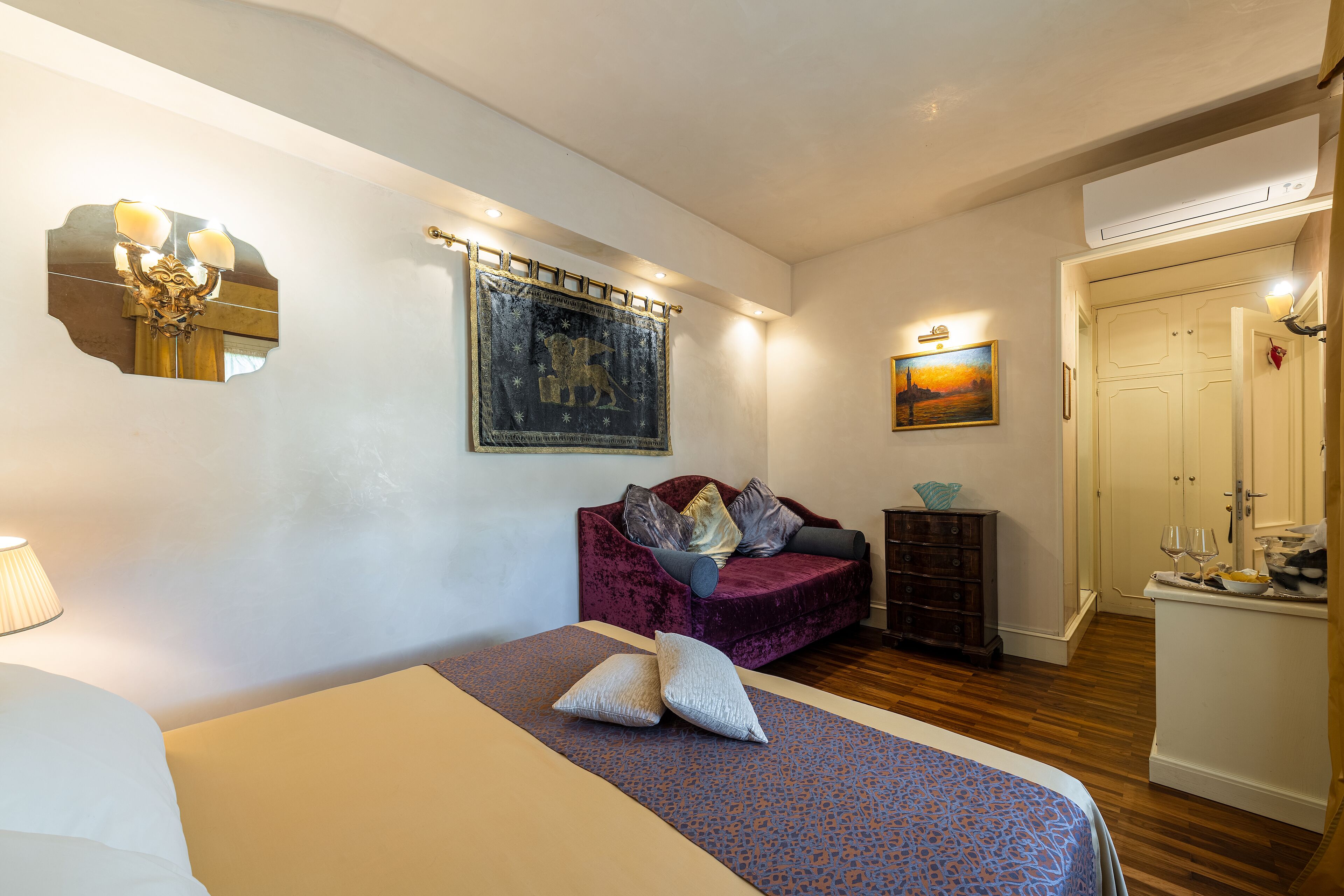 A bedroom with a bed, a purple sofa, a dresser, and a painting on the wall.