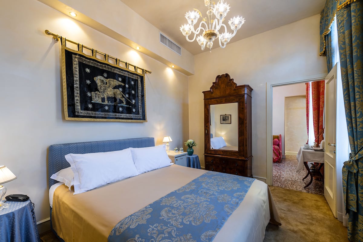A hotel room with a large bed, a chandelier, a wooden dresser, and a mirror.