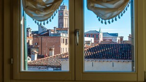 Vista a través de una ventana con cortinas, mostrando un paisaje urbano con una torre destacada y diversos edificios.