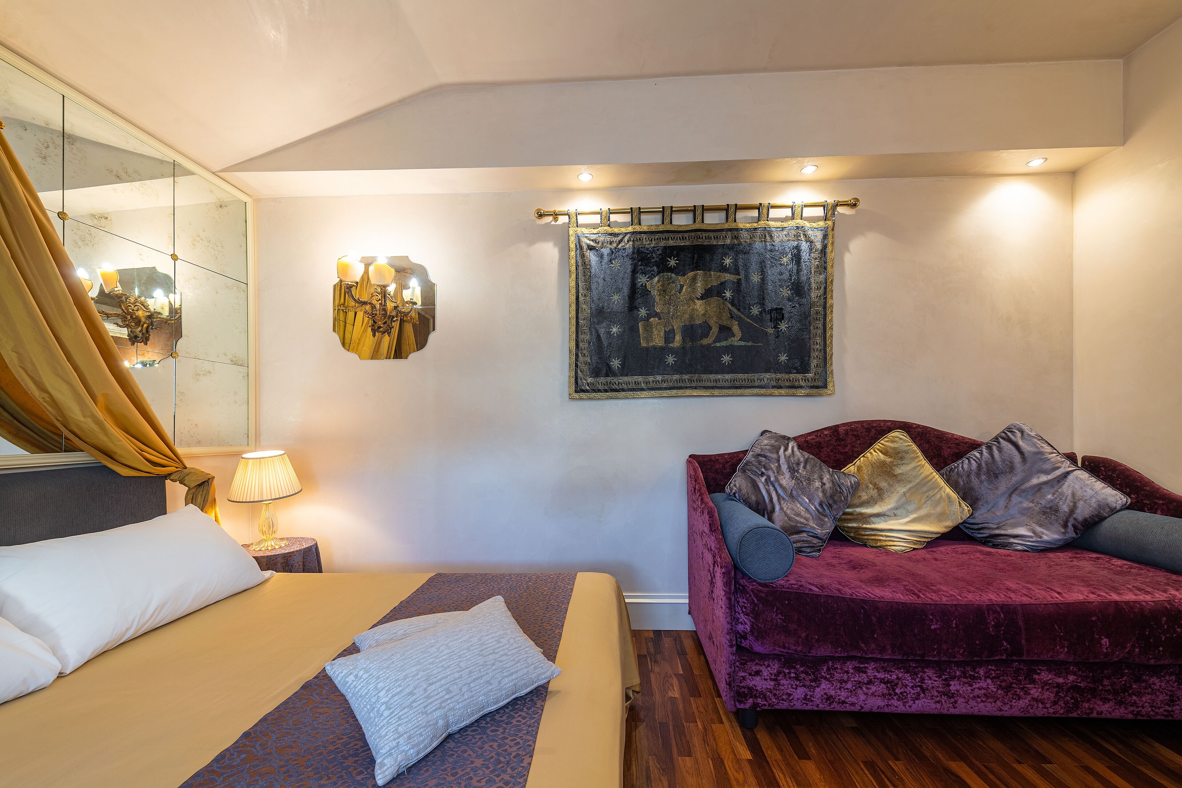 Une chambre d’hôtel avec un lit, un canapé, une lampe fixée au mur et un tableau encadré.