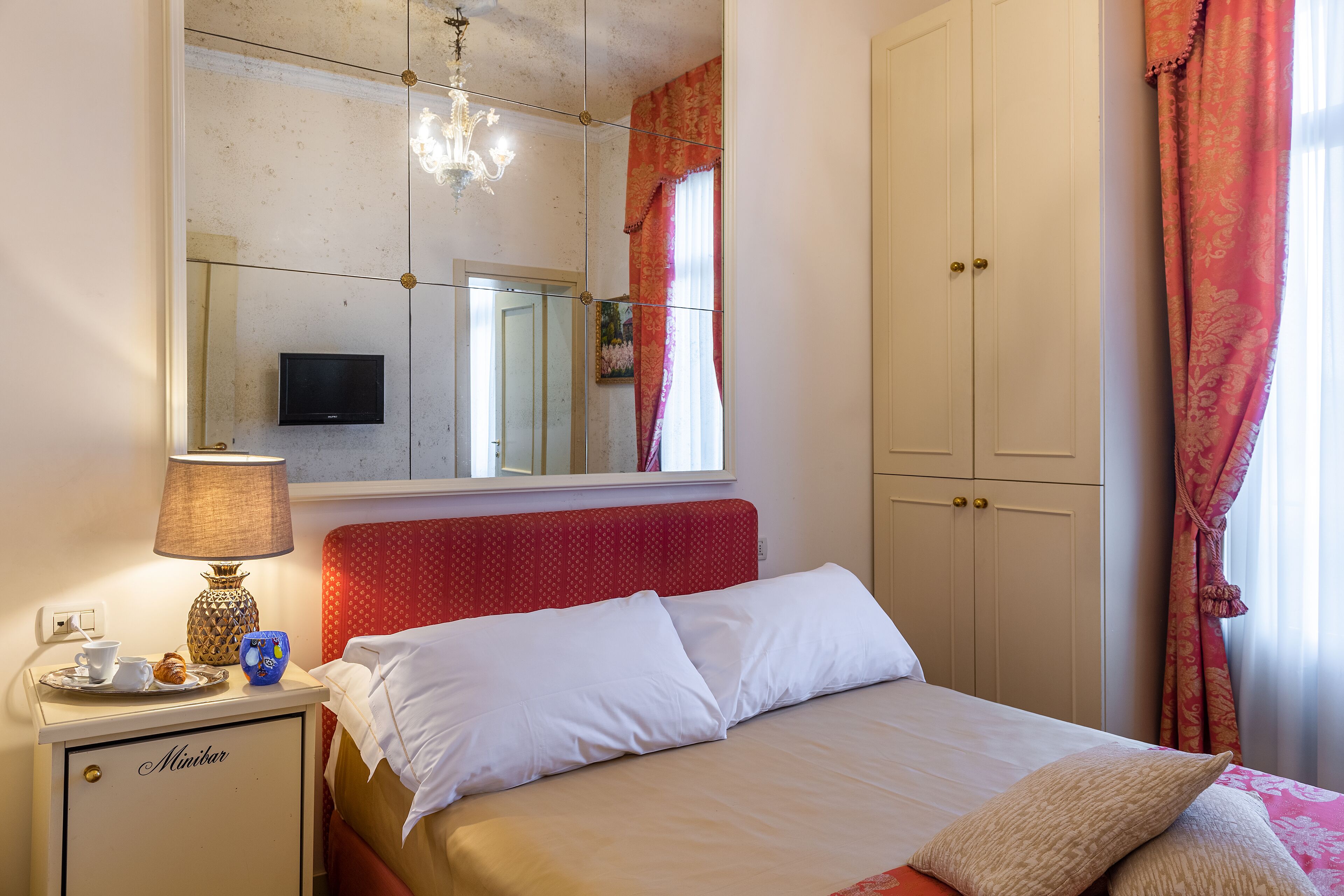 Een slaapkamer met een bed, nachtkastje met lamp, televisie en een kledingkast.