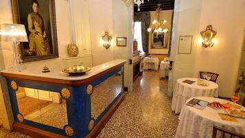 A hotel lobby with a reception desk, a large portrait, and tables with food and drinks.
