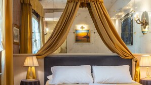 Habitación de hotel con cama, dos mesitas de noche, dosel sobre la cama, un cuadro en la pared y un candelabro.