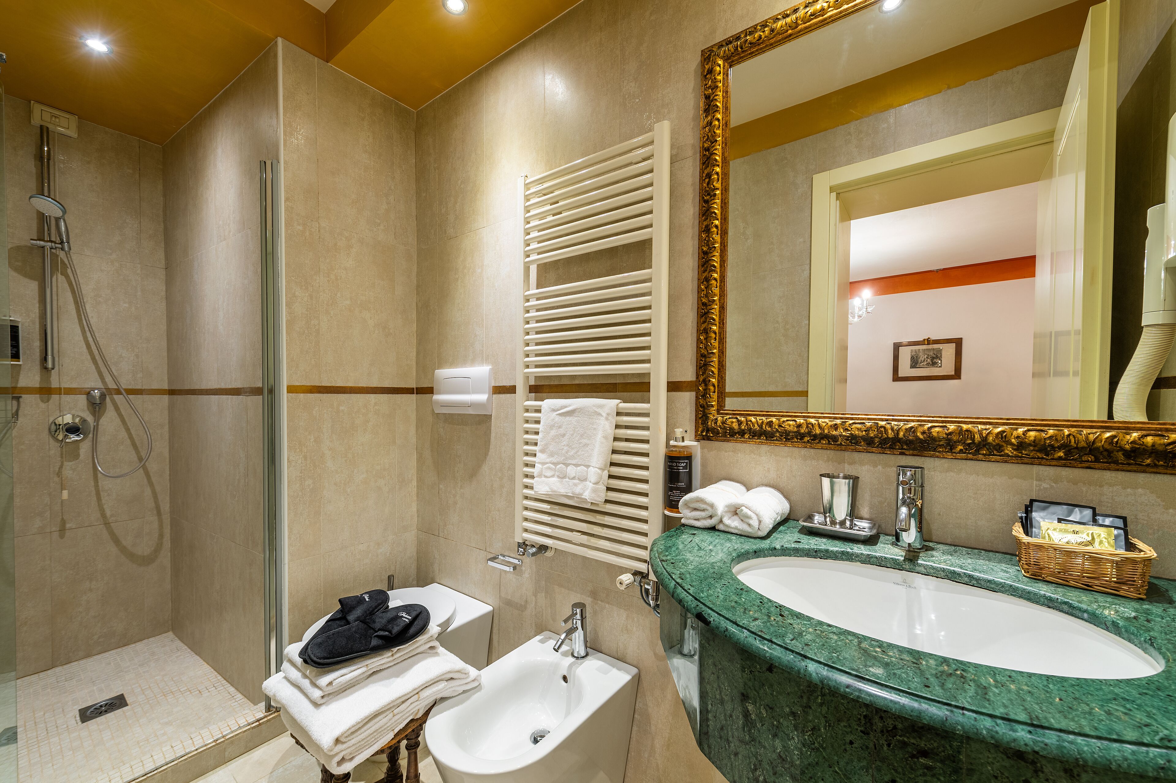 A modern bathroom with a glass-enclosed shower, a sink with a marble countertop, and a large mirror with a gold frame.