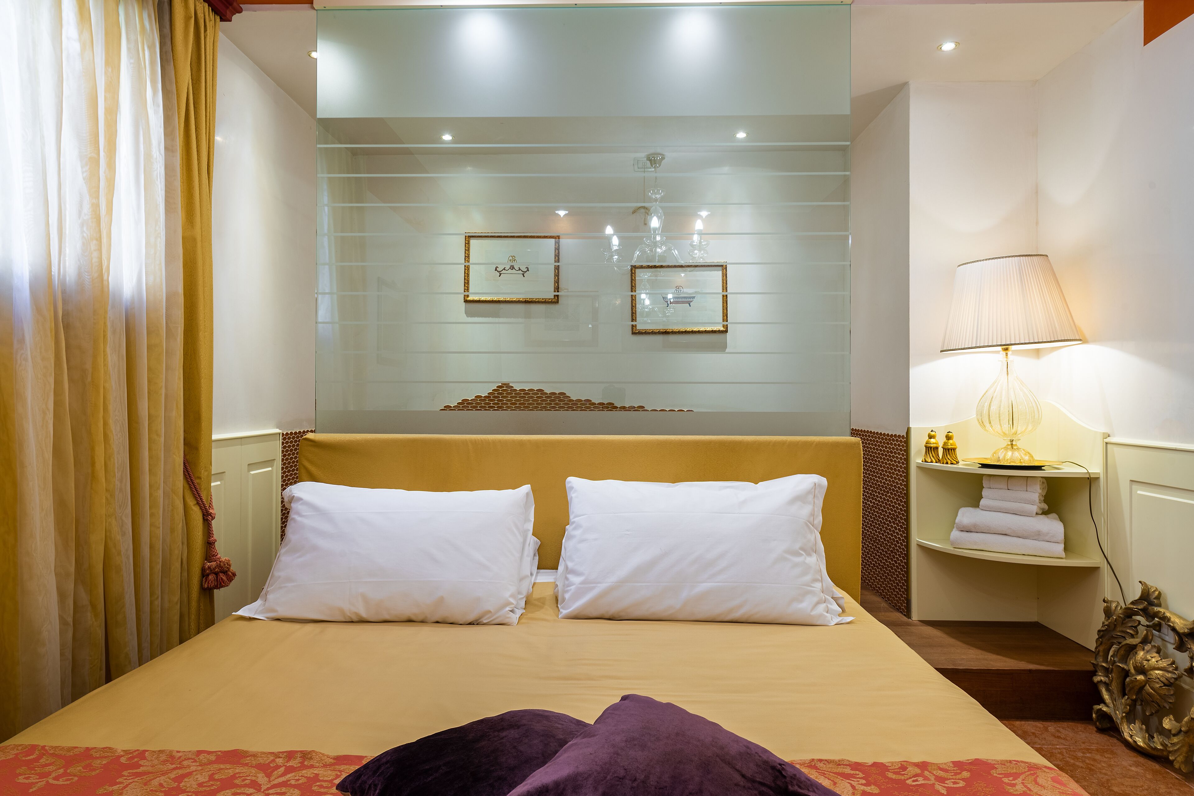 A hotel room with a bed, a nightstand with a lamp, and a mirror above the bed.