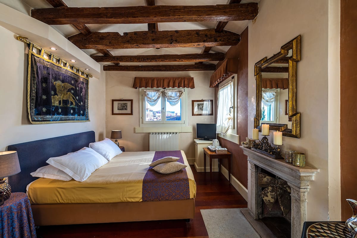 A bedroom with a large bed, a desk with a computer, a fireplace, and a mirror.
