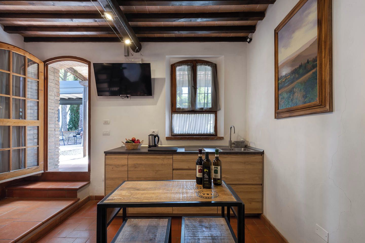 A kitchen with a wooden table, a TV mounted above it, and a window with curtains.