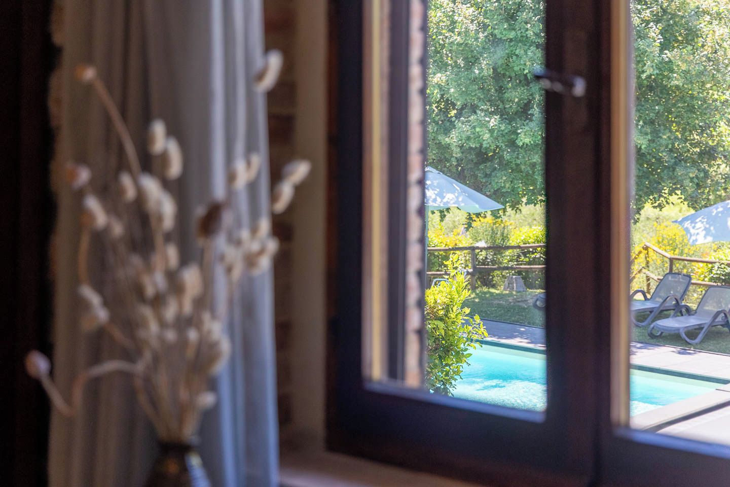 Vista dalla finestra su una zona piscina con lettini e un pontile in legno.