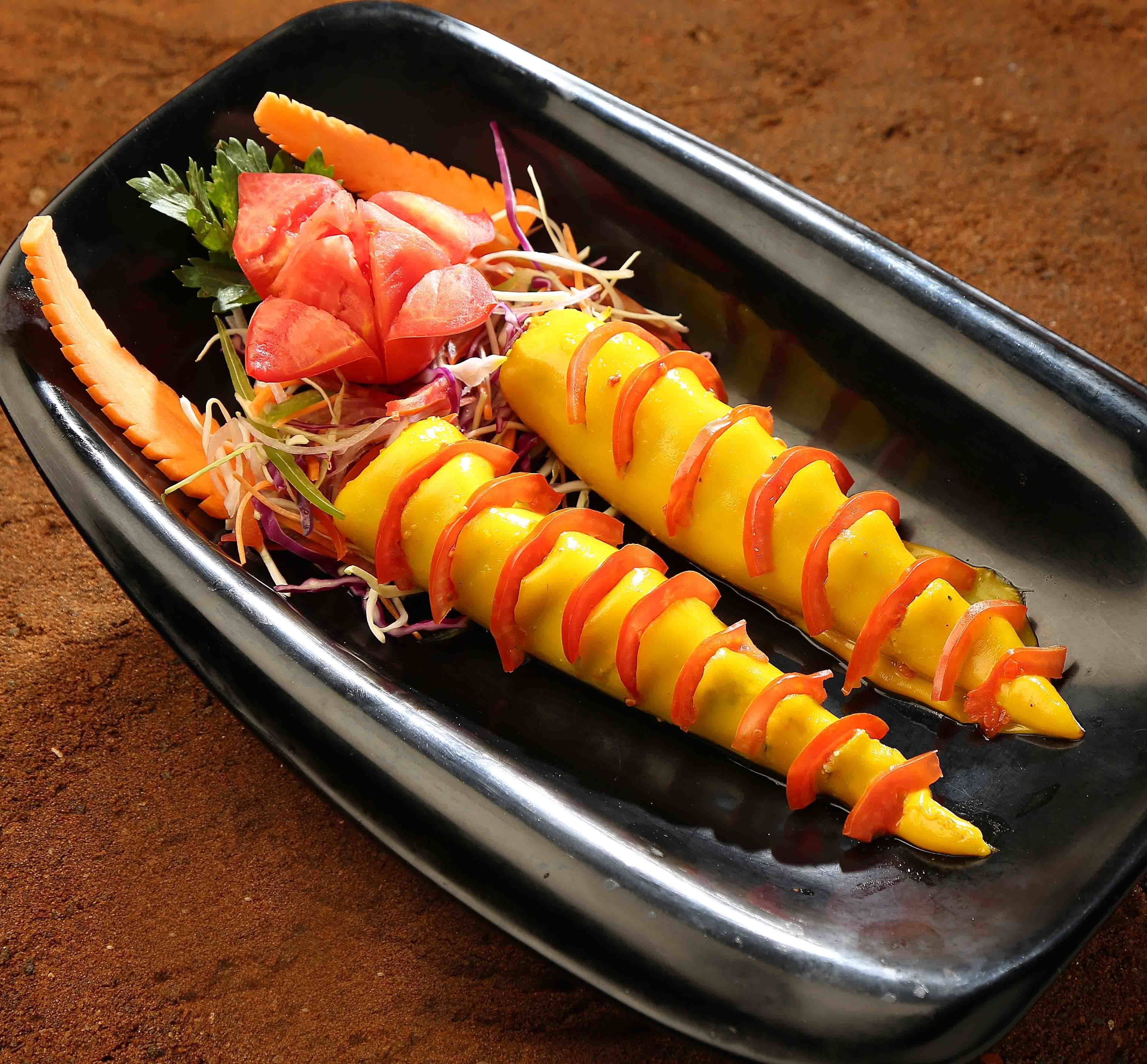 A dish with yellow and orange elements, garnished with red strips and green leaves.